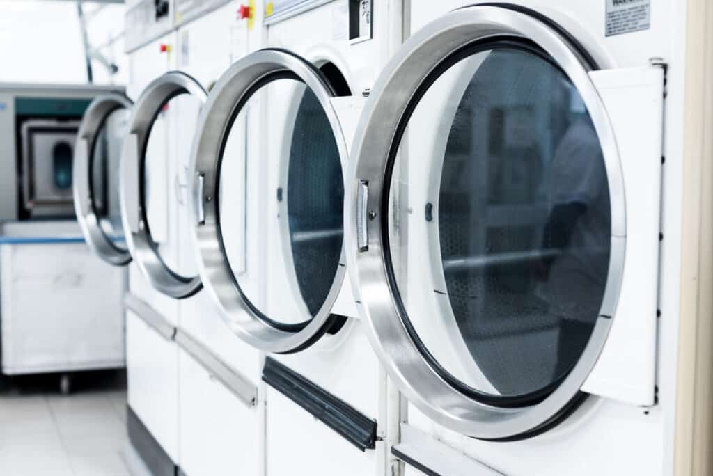 Alignement de machines à laver et sèche-linge industriels blancs dans une blanchisserie professionnelle.